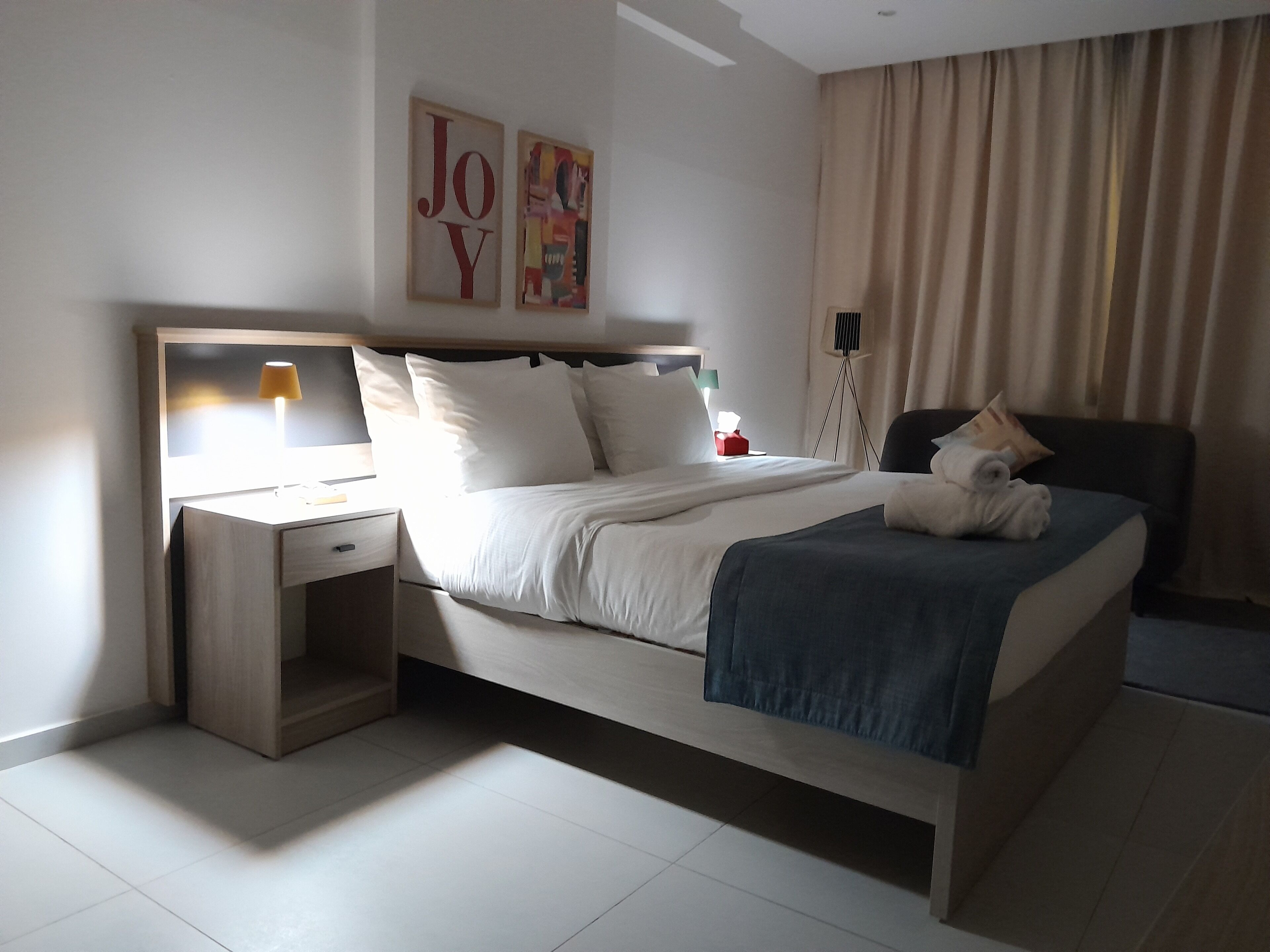 Ein modernes Hotelzimmer mit Bett, Nachttisch, Lampe und Kunstwerk an der Wand.