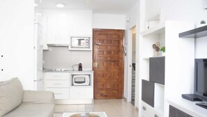 A compact living space with a kitchenette, a wooden door, a TV, and a small table with a remote control. - MONKÓ ROSARIO´S APARTMENT BEACH & SUN (Torremolinos)