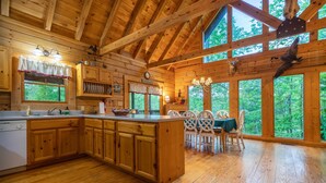 L’intérieur d’un chalet en bois comprend une grande cuisine, un coin repas et de grandes fenêtres qui offrent une vue sur la forêt.