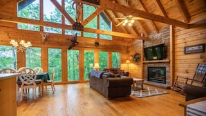 L’intérieur d’un chalet en bois comprend une cheminée, un téléviseur et un coin repas avec des chaises et une table.