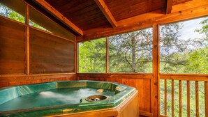 Une cabane en bois dotée d’un bain à remous, de grandes fenêtres et offrant une vue sur la forêt.