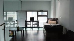 A modern living room with a sofa, a small table, and a TV. There is a balcony with a glass door and a chair outside. - Amaizing Loft in Madrid Norte (Madrid)
