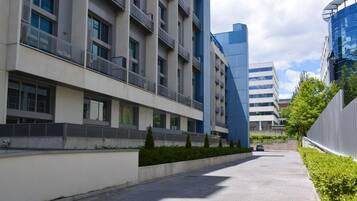 Un edificio moderno con fachada limpia y geométrica, un sendero pavimentado y un pequeño espacio verde con arbustos.