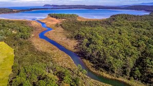 Een rivier kronkelt door een bebost landschap, met een uitzicht op verre heuvels en een groot wateroppervlak.
