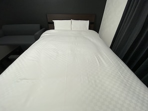 Relax in a serene space with a neatly made bed, a comfortable armchair, and a dark headboard.