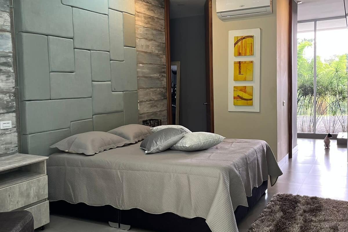 Ein modernes Schlafzimmer mit einem Bett, einer grauen Sitzbank, einem grauen Teppich und einer Wand-Klimaanlage.