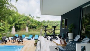 Un espace piscine extérieur moderne, doté de chaises longues, d’une table en bois et d’équipements de musculation.