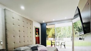 Une chambre moderne dotée d’un grand lit, d’un téléviseur à écran plat fixé au mur et d’une porte-fenêtre coulissante donnant sur un espace extérieur.