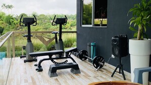 Un espace de remise en forme extérieur abrité, équipé d’appareils d’exercice, d’une table en bois et d’une plante en pot.