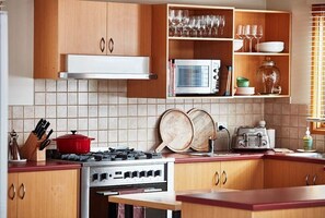 Kitchen equipped with a stove, microwave, and toaster oven, along with ample storage and a shelf.