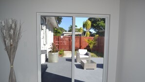 Vista a través de una puerta corredera de vidrio a un patio con mobiliario exterior y una planta en maceta.