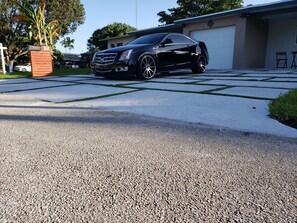 A black luxury car parked in a driveway with a modern house in the background.