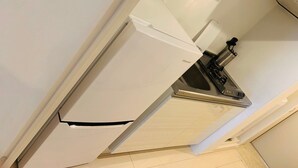Pieni, käytännöllinen keittiö, jossa on valkoinen jääkaappi, liesi ja pesuallas.