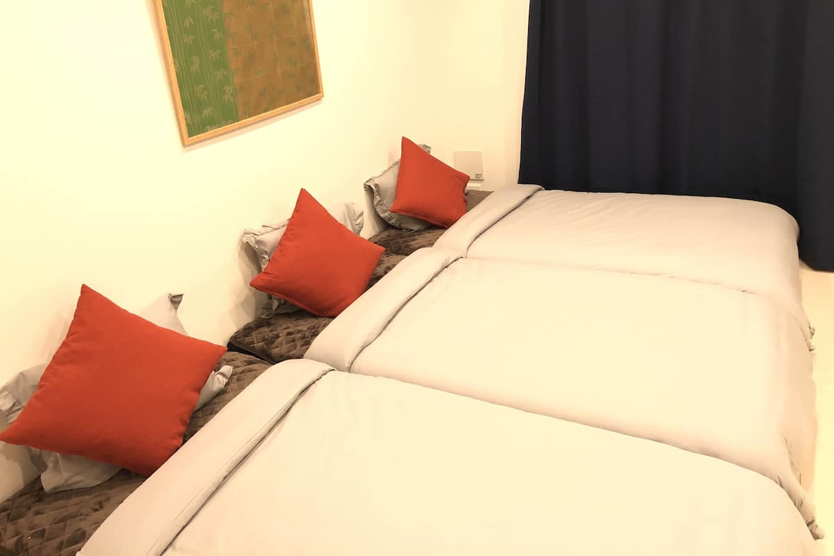 A bed with white bedding and red pillows, a framed artwork on the wall, and a dark curtain.