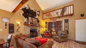 A cozy living room with leather sofas, a stone fireplace, a mounted animal head, and a wooden staircase.