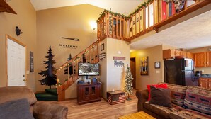 A cozy living room with a wooden staircase, a television, a Christmas tree, and a sofa with patterned cushions.