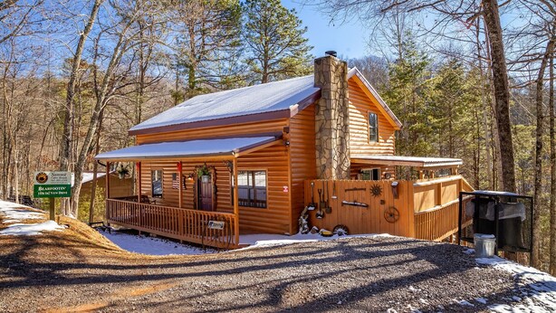 A log cabin with a stone chimney, a porch, and a gravel driveway.