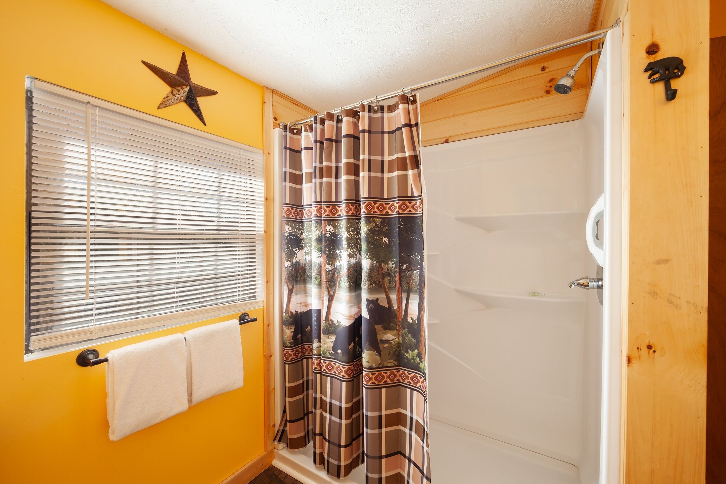 A bathroom with a shower curtain featuring a forest scene, a star decoration on the wall, and a window with blinds.