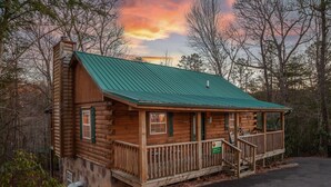 A log cabin with a green metal roof, a porch, and a small staircase leading to the entrance. - Sleepin' Inn 2 Bedroom Cabin by RedAwning (Sevierville)