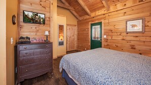 A cabin-style bedroom with a wooden ceiling, a bed with a patterned bedspread, a dresser, a television mounted on the wall, and a framed picture on the wall. - Sleepin' Inn 2 Bedroom Cabin by RedAwning (Sevierville)