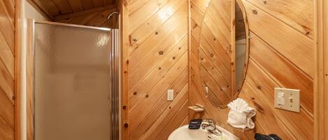 Un baño revestido de paneles de madera con cabina de ducha de vidrio, un lavamanos y un espejo.