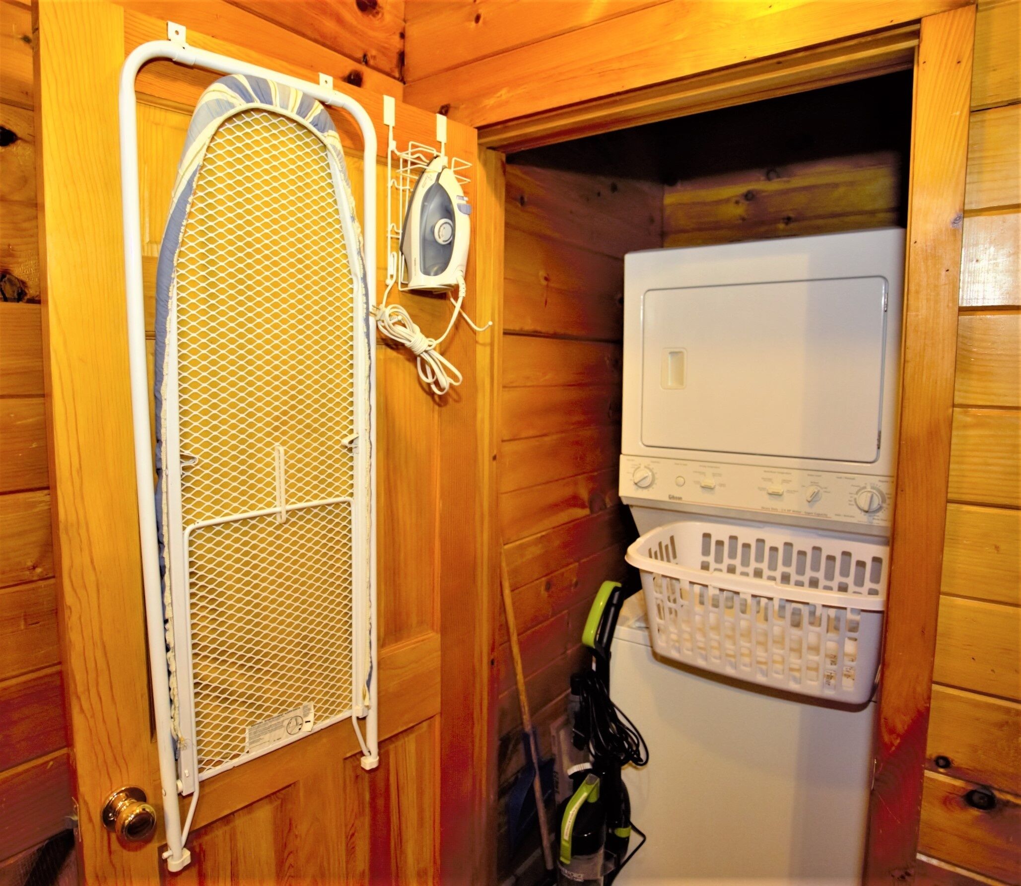 A compact room with a wooden interior, featuring a washing machine and a drying rack.