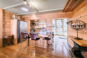 Una cocina moderna con paredes de madera, un refrigerador de acero inoxidable, una mesa de comedor de madera con taburetes tipo barra y un ventanal que proporciona luz natural.
