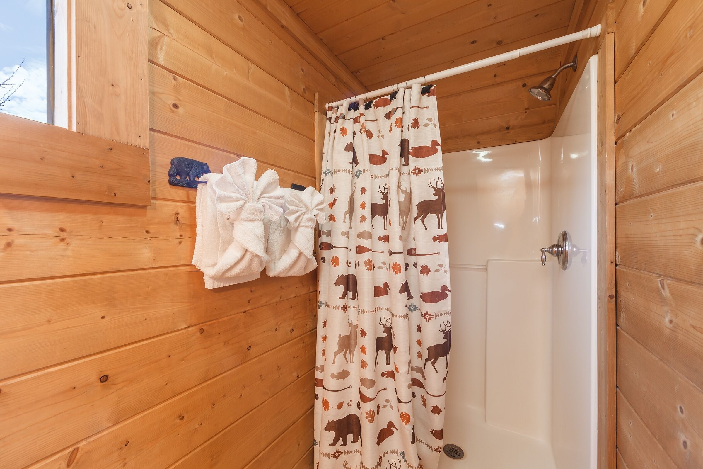 Ein Badezimmer einer Holzhütte mit einer Duschvorhang mit Tiermotiven, einer weißen Badewanne und einem Handtuchhalter mit einem weißen Handtuch.