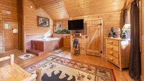 A log cabin interior with a wooden floor, a fireplace, a television, a wooden dresser, and a ceiling fan. - Something Extra 2 Bedroom Cabin by RedAwning (Sevierville)