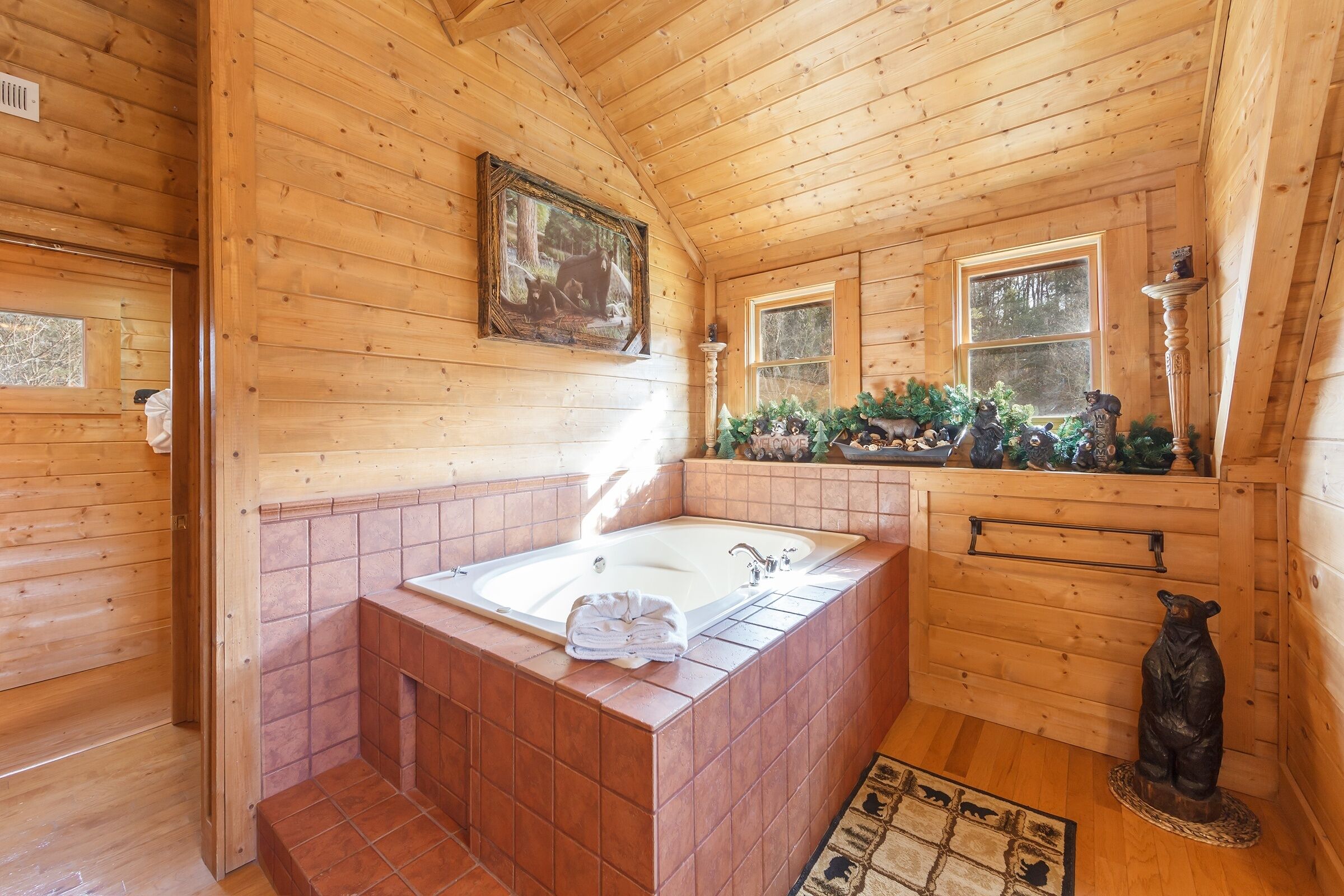 A wooden cabin bathroom with a large bathtub, a framed picture on the wall, and a bear statue.