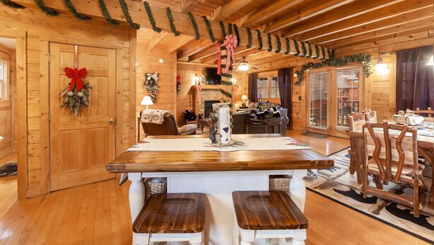 A cozy cabin interior with a wooden interior, a central island with stools, a fireplace, and holiday decorations. - Something Extra 2 Bedroom Cabin by RedAwning (Sevierville)