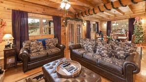 A cozy log cabin interior with two leather sofas, a wooden coffee table, and a ceiling fan. - Something Extra 2 Bedroom Cabin by RedAwning (Sevierville)