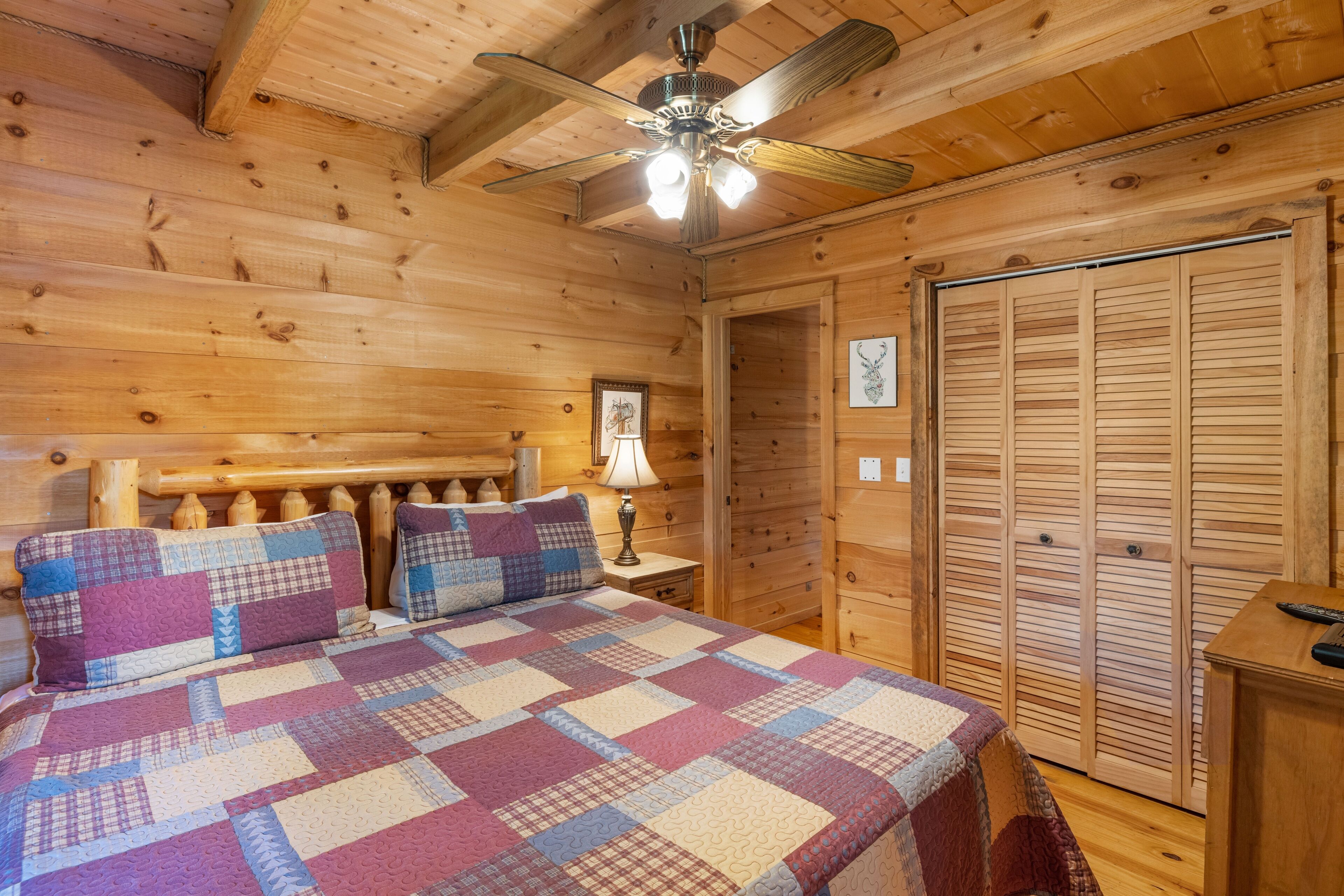 A wooden cabin bedroom with a bed, a nightstand, a ceiling fan, and a wooden closet.