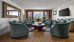 Ein modernes Wohnzimmer mit großem Fenster, einem Flachbildfernseher und einem farbenfrohen Teppich.