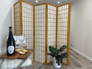 A room with a glass table, a bottle, glasses, crackers, and a potted plant.