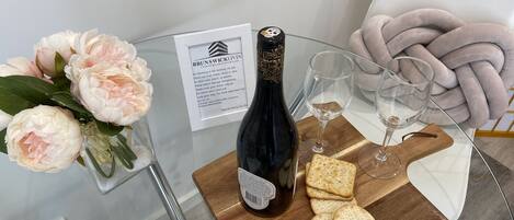 Una mesa de vidrio con una botella de vino, copas, galletas y un ramo de flores.