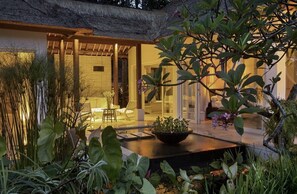 A modern outdoor area with a thatched roof, a seating area with a table and chairs, and a variety of plants.