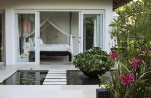 A bedroom with a bed, a bedside table, and a window with a view of the garden.