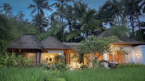 A thatched-roof bungalow with a veranda, surrounded by lush greenery and palm trees. - Ubud's Hidden Gem: Experience Luxury in Nature's Lap, Near the gates of Ubud. (Ubud)