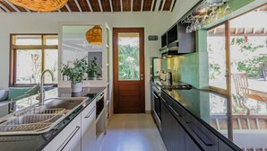 Uma cozinha moderna com pia, fogão e armários. Há uma porta que dá para uma varanda com vista para o verde.