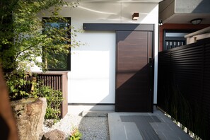 A modern entrance with a dark wooden door, a small window, and a gravel pathway leading to a wooden deck. - Onya Kaede (Kyoto)