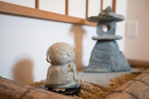 A small ceramic Buddha statue on a cushion with a stone pagoda in the background. - Onya Kaede (Kyoto)