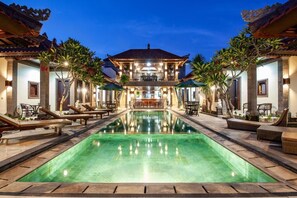 A pool area with lounge chairs and umbrellas, a central pool, and a building with traditional architecture. - Grand Yuma Hotel & Villa (Denpasar)