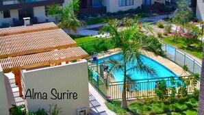 A rooftop pool area with a wooden pergola, surrounded by lush greenery and palm trees. - Apartment Alma Surire pool view (Arica)