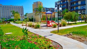 A hotel courtyard with a playground, palm trees, and a well-maintained garden.