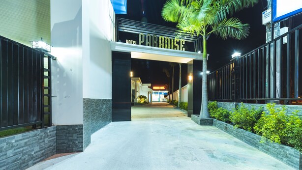 Ein Hotel mit Eingangsbereich, einem Schild mit der Aufschrift 'PARADISE HOTEL', einem gepflasterten Weg und einer Palme.