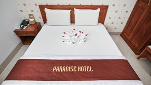 Ein ordentlich bezogenes Bett mit einer weiß-roten Tagesdecke, einem floralen Wanddesign und einem Holz-Kopfteil.