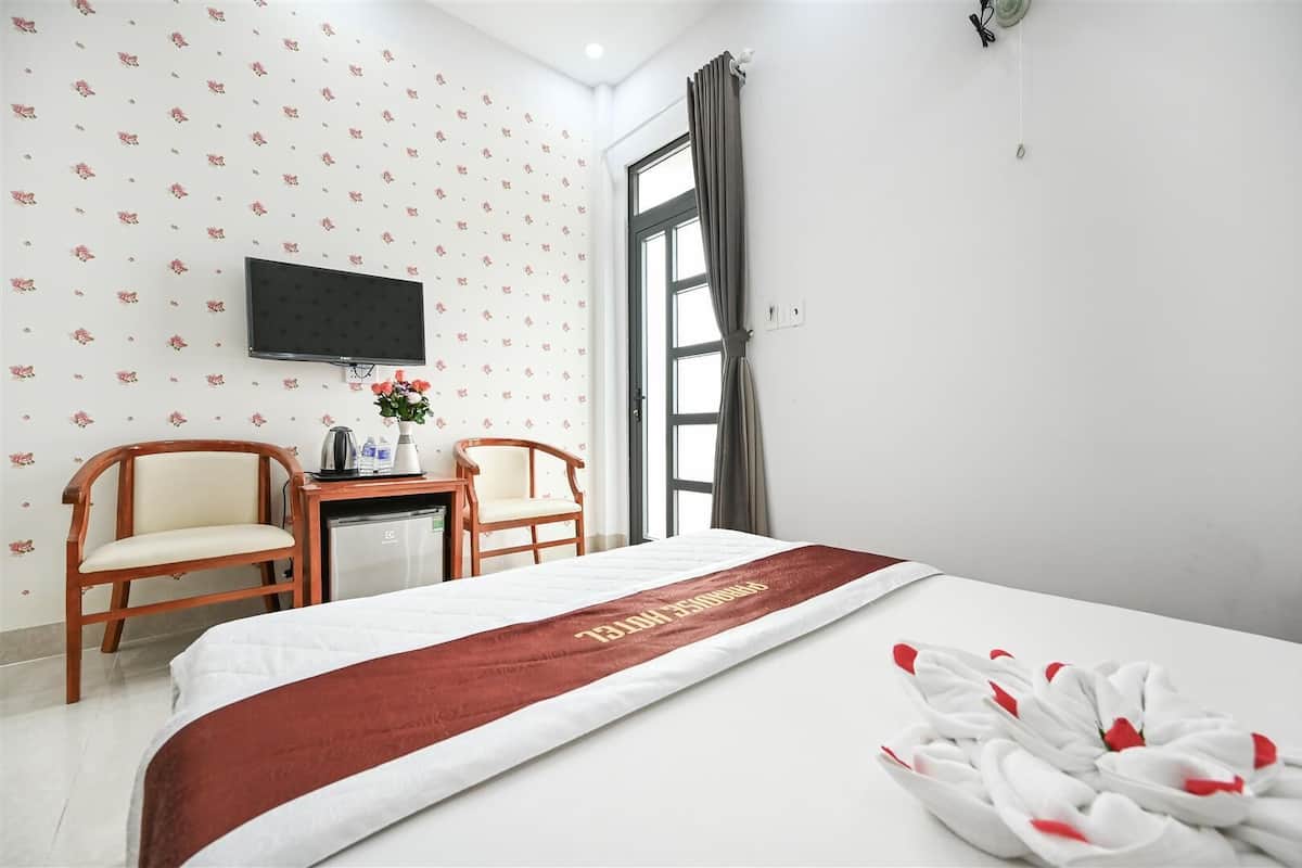 A hotel room with a bed, two chairs, a desk, a flat-screen TV, and a window with curtains.