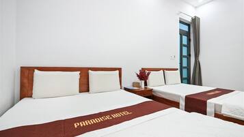 A hotel room with two beds, each with a wooden headboard and white bedding. A red and gold bed runner with the text "PARADISE HOTEL" is visible.