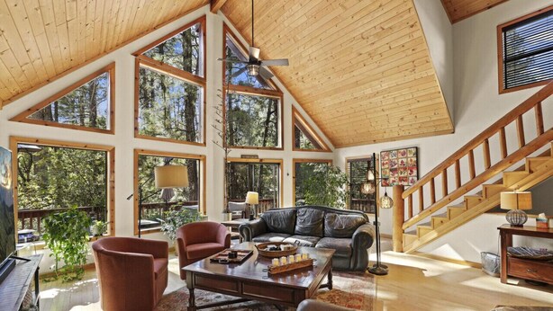 A spacious living room with a high ceiling, large windows, a wooden staircase, and a cozy seating area. - Chalet Forest Views, 2 kings, fireplace, decks (Pine)